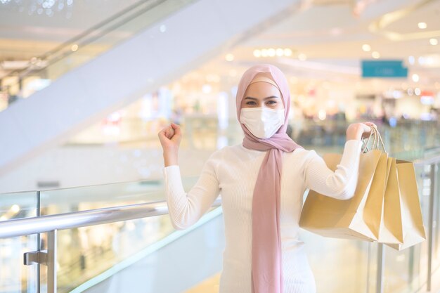 Una giovane donna musulmana che indossa una maschera protettiva nel centro commerciale, che fa shopping sotto il concetto di pandemia di covid-19.