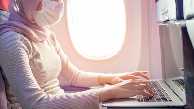 Young muslim woman with hijab wearing face mask onboard New normal travel after covid19