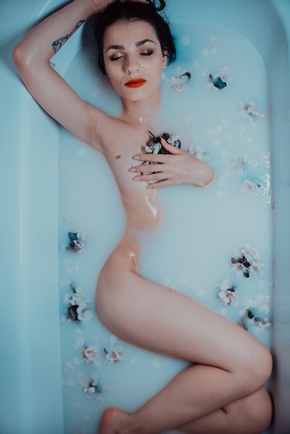 Молодая обнаженная девушка наслаждается и отдыхает в ванне с молоком и яблочными цветами