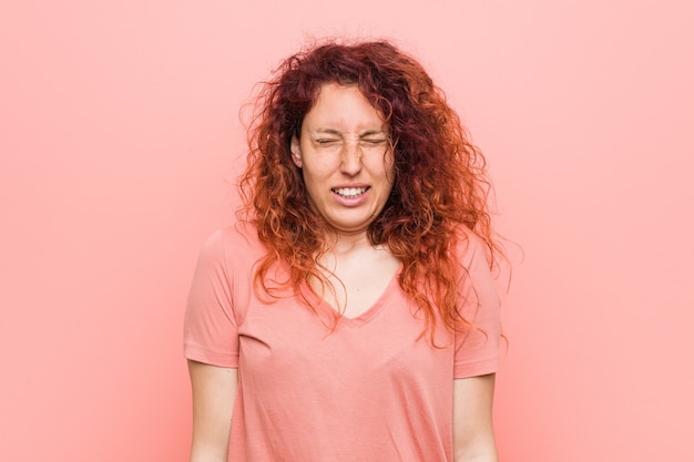 Young natural and authentic redhead woman laughs and closes eyes, feels relaxed and happy.