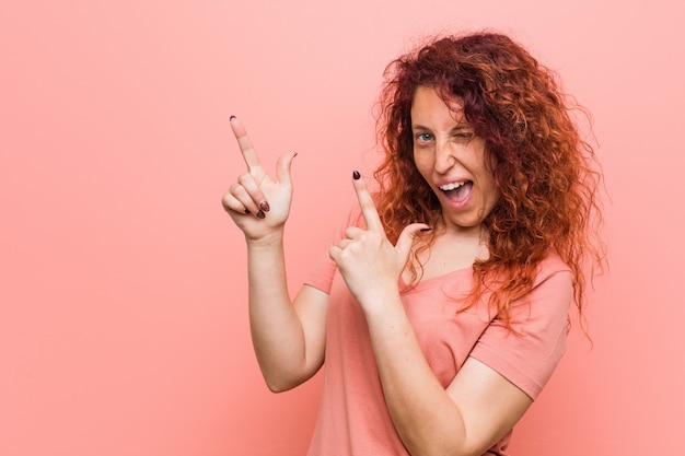 Young natural and authentic redhead woman pointing with forefingers to a copy space
