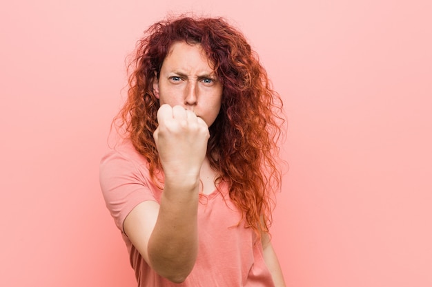 Giovane donna rossa naturale e autentica che mostra il pugno con con espressione facciale aggressiva.