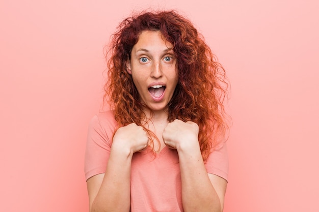 Young natural and authentic redhead woman surprised pointing with finger, smiling broadly.