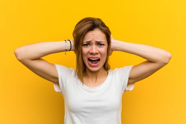 Young natural caucasian woman covering her ears with hands trying not to hear too loud sound.