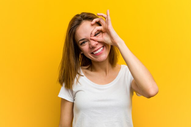 Young natural caucasian woman excited keeping ok gesture on eye.