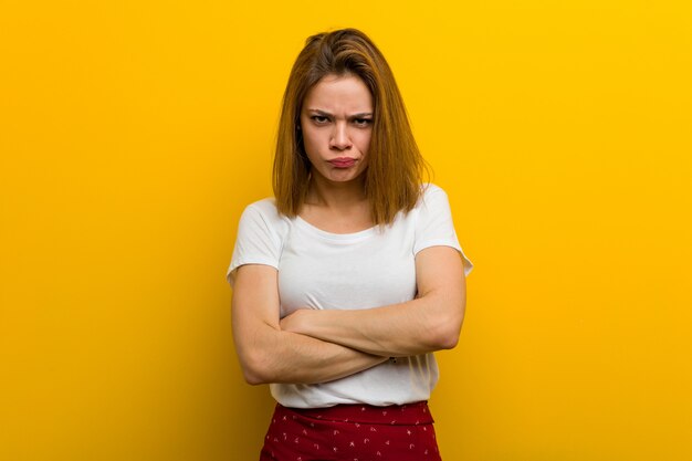 Young natural caucasian woman frowning her face in displeasure, keeps arms folded.