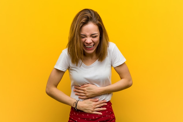 Young natural caucasian woman laughs happily and has fun keeping her hands on stomach.