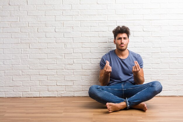 Young natural man sit on a wooden floor sad and depressed, making a gesture of need, restoring to charity, concept of poverty and misery