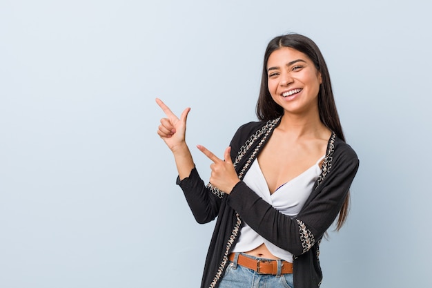 Young natural and pretty arab woman pointing with forefingers to a copy space, expressing excitement and desire.