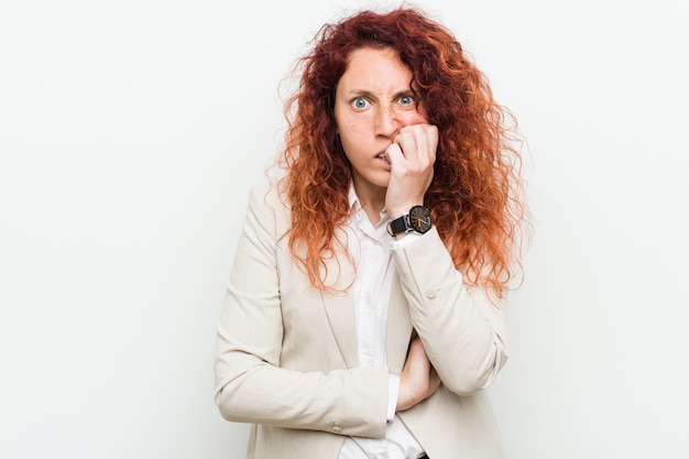 Young natural redhead business woman isolated against white wall biting fingernails, nervous and very anxious.