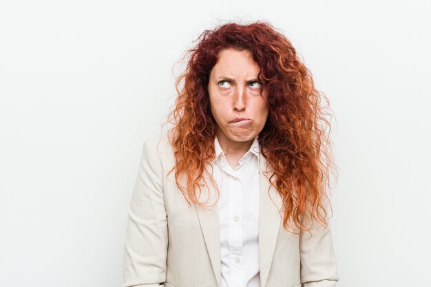 Young natural redhead business woman isolated on white confused, feels doubtful and unsure.