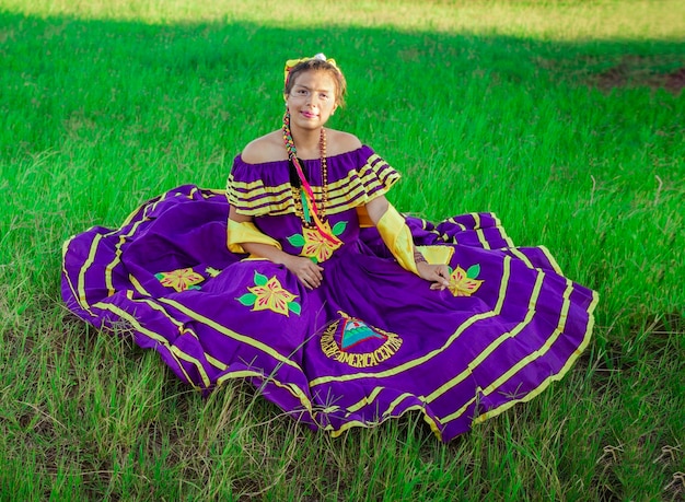 Молодая никарагуанка в традиционном народном костюме сидит на траве в поле Портрет никарагуанки в народном костюме сидит на траве