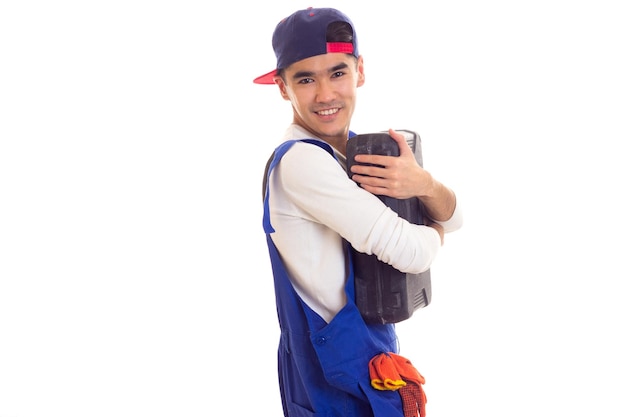 Young nice man in white shirt and blue overall with orange gloves and blue snapback holding toolbox