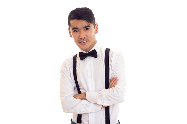 Young nice man in white shirt with black bowtie and black suspenders on white background in studio