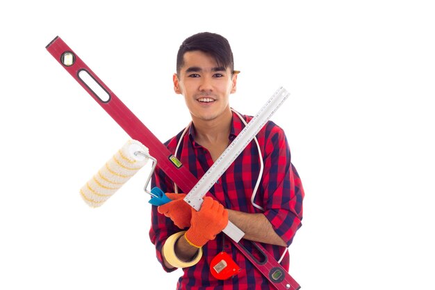 Young nice man with dark hair in red plaid shirt holding red level tapemeasure white roll and ruler