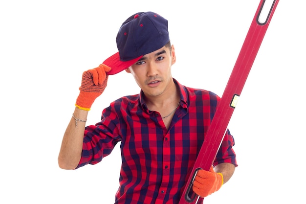 Young nice man with dark hair in red plaid shirt with gloves and blue snapback holding red level