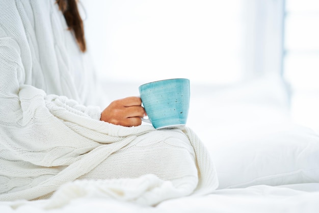 コーヒーまたは紅茶のマグカップとベッドで若い素敵な女性