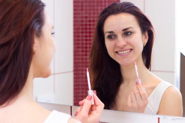 Young nice woman lip glossing in front of the mirror in her\
burgundy bathroom