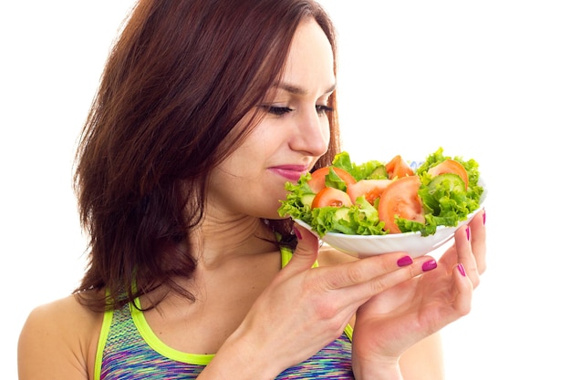 Young nice woman wearing in colored sports top holding a fork and plate with green salad and tomato