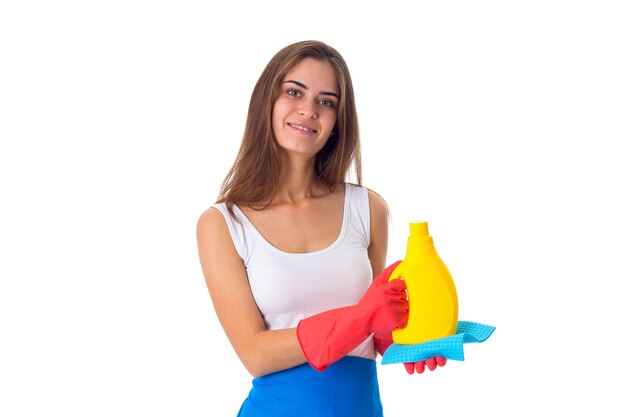 Young nice woman in white shirt and blue apron with red gloves holding duster and detergent