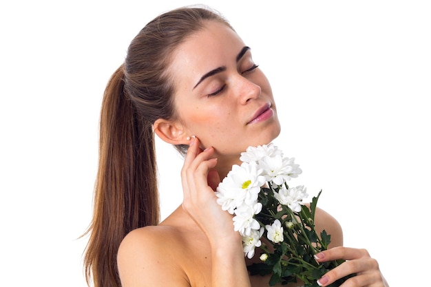 Young nice woman with long brown ponytail holding white flowers on white background in studio