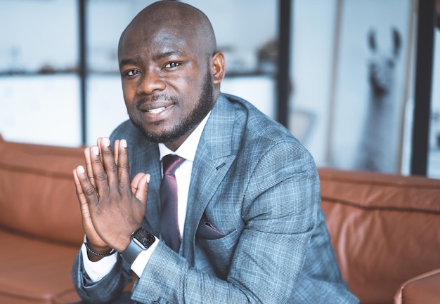 Young nigerian guy in a formal suit sits with folded hands and gazes at front