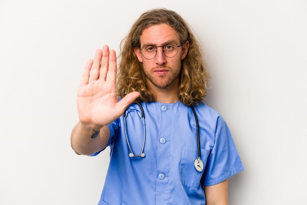 青の背景に孤立した若い看護師の白人男性は、あなたを妨げる一時停止の標識を示す伸ばした手で立っています
