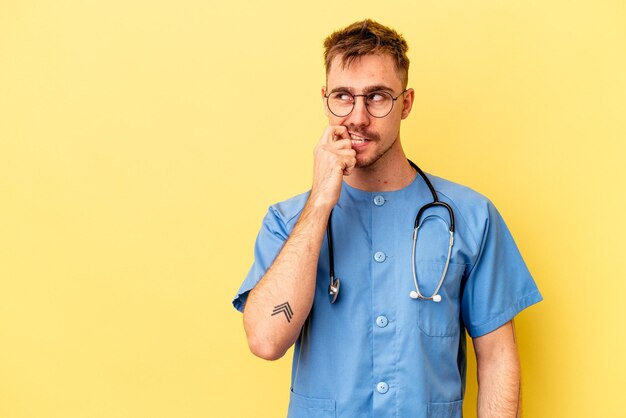 Young nurse caucasian man isolated on yellow background relaxed thinking about something looking at a copy space.