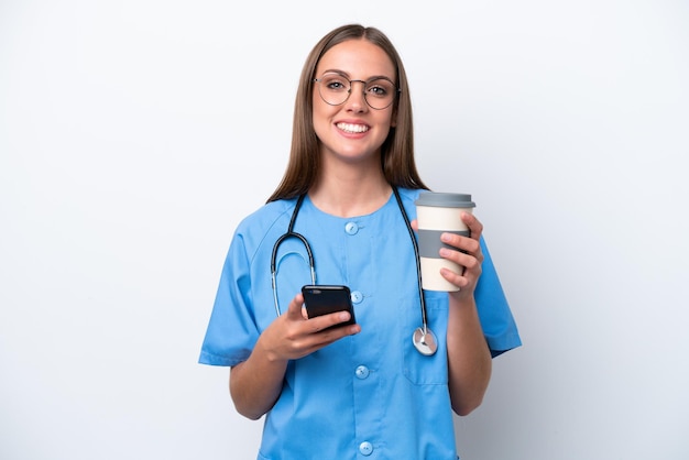 Young nurse caucasian woman isolated on white background holding coffee to take away and a mobile