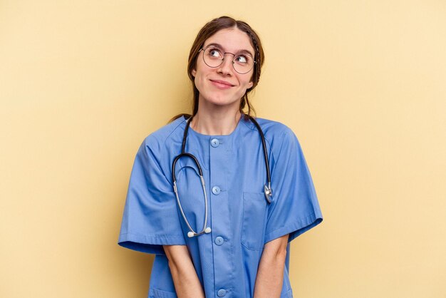 Young nurse caucasian woman isolated on yellow background dreaming of achieving goals and purposes