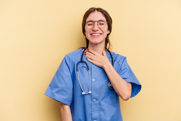 Young nurse caucasian woman isolated on yellow background laughs out loudly keeping hand on chest