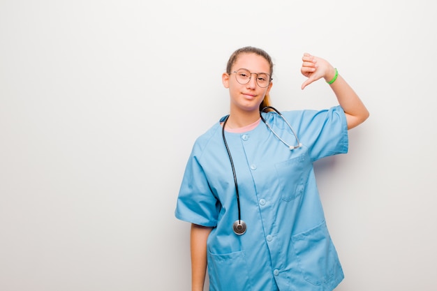 Young nurse feeling proud, arrogant and confident, looking satisfied and successful, pointing to self against white wall