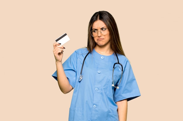 Young nurse holding a credit card on isolated yellow background