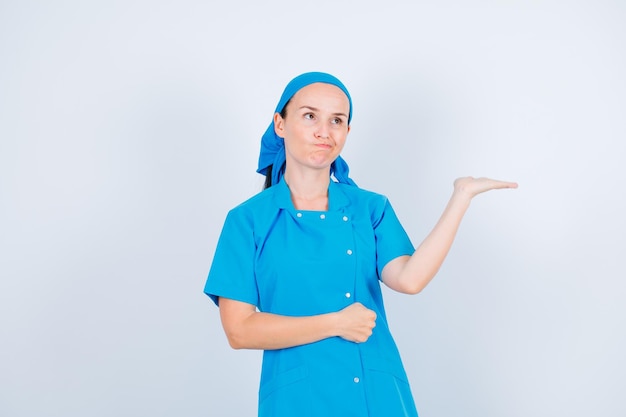 Young nurse is thinking by looking up and pointing left with hand on white background