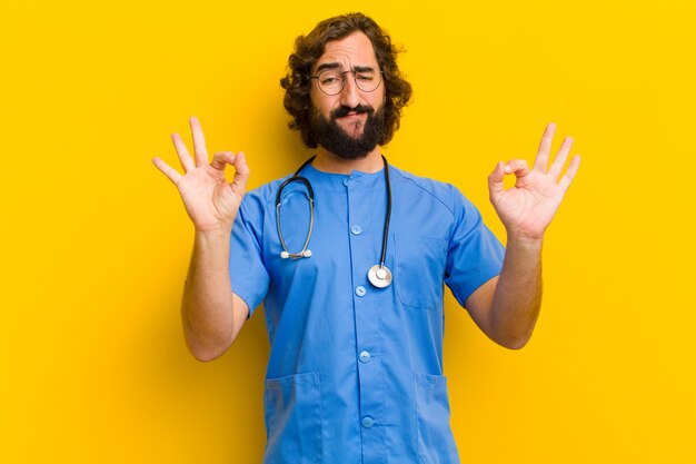 Young nurse man okay gesture against yellow wall