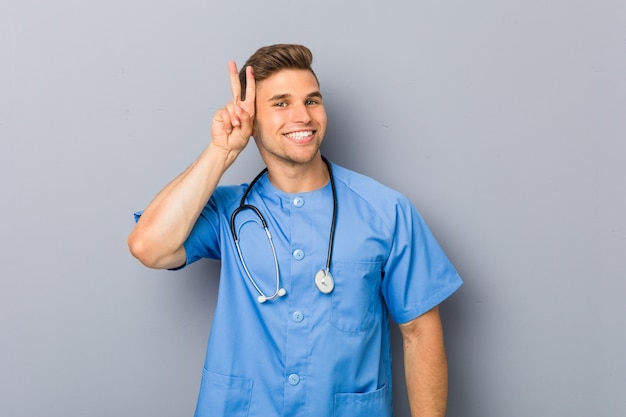 Young nurse man showing victory sign and smiling broadly.