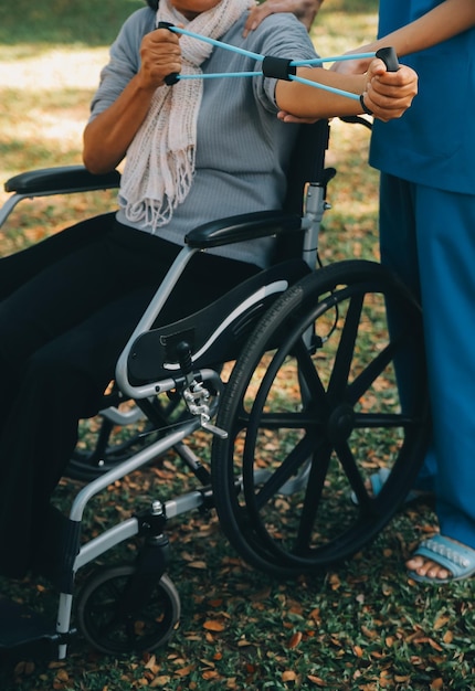 Молодая медсестра или физиотерапевт в комбинезоне помогает счастливой пенсионерке заниматься фитнес-упражнениями с помощью легких гантелей дома Концепция физиотерапии для пожилых людей