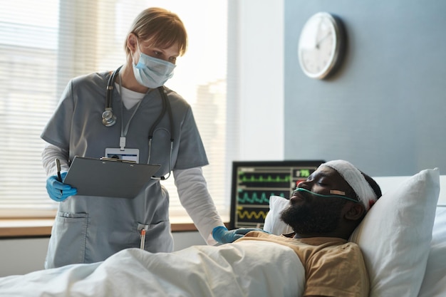 Young nurse in protective mask bending over injured soldier