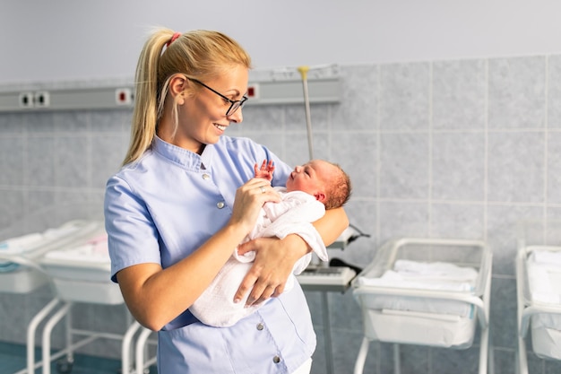 Giovane infermiera in piedi nel reparto maternità e tiene in braccio il neonato. dopo il concetto di nascita.