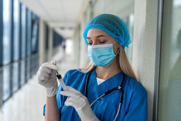 Foto giovane infermiera in uniforme e maschera che tiene una siringa nelle sue mani sul corridoio