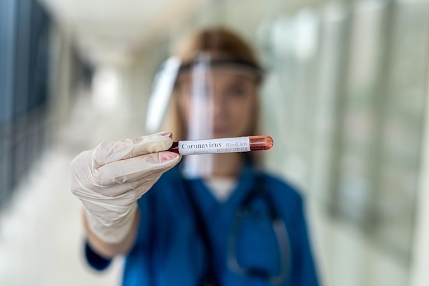 A young nurse in a uniform with a protective cap holds a blood sample on a covid. Medicine concept