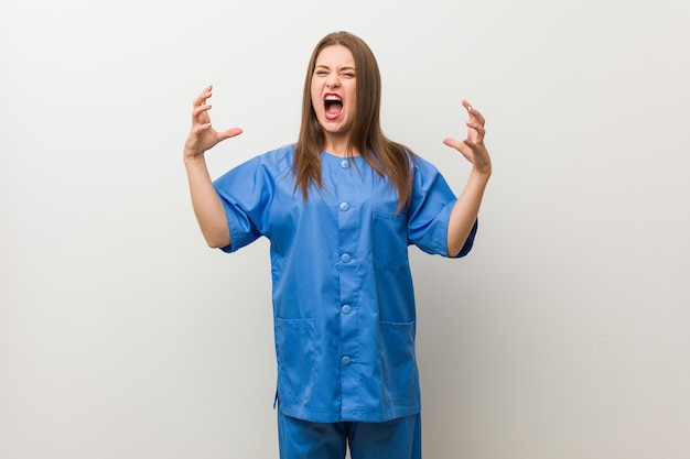 Photo young nurse woman against a white wall screaming with rage.