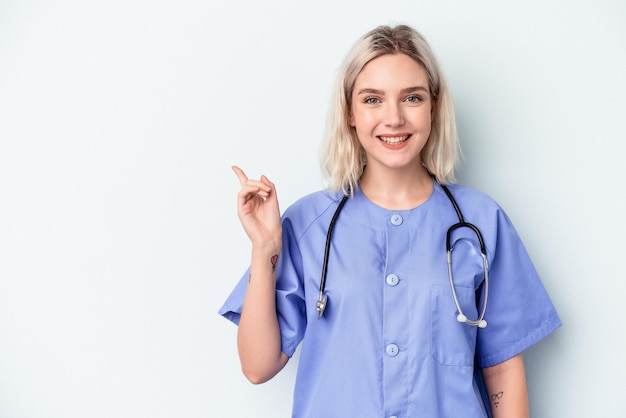 Young nurse woman isolated on blue background smiling and pointing aside, showing something at blank space.