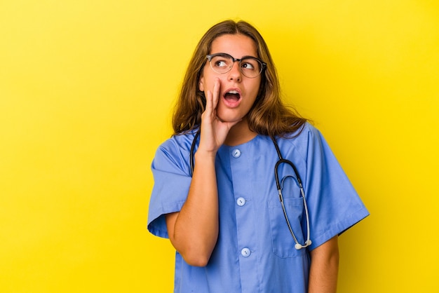 Young nurse woman isolated on yellow background  is saying a secret hot braking news and looking aside