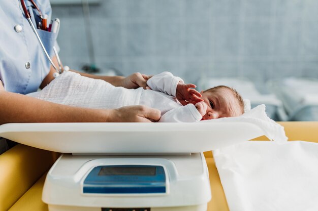 Young nurse working in maternity ward. She measuring weight and wrapping the newborn baby.