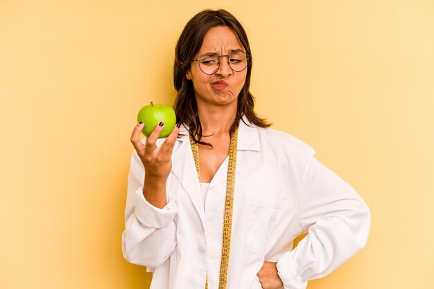 Young nutritionist woman holding a weighing machine isolated on yellow background