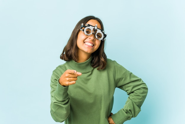 Young oculist latin woman over isolated wall cheerful smiles pointing to front.