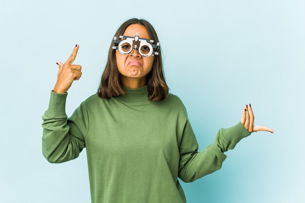 Young oculist latin woman over isolated wall holding and showing a product on hand.