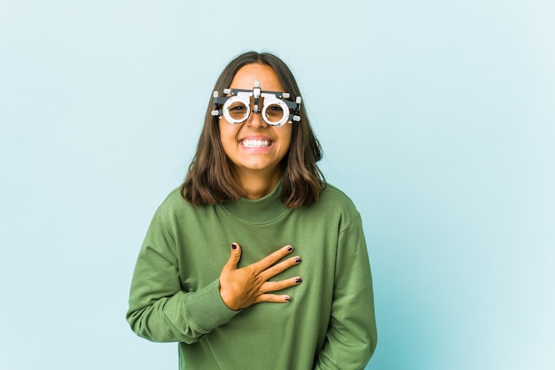 Young oculist latin woman over isolated wall laughs out loudly keeping hand on chest.