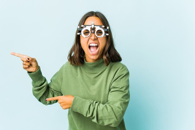 Young oculist latin woman over isolated wall pointing with forefingers to a copy space, expressing excitement and desire.